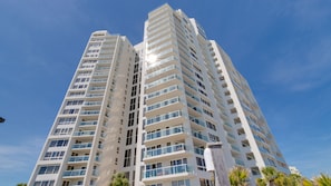 A high-rise building with multiple balconies, large windows, and a clear sky.