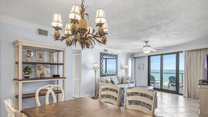 Uma sala de jantar com mesa e cadeiras de madeira, um lustre e vista para o oceano através de grandes janelas.