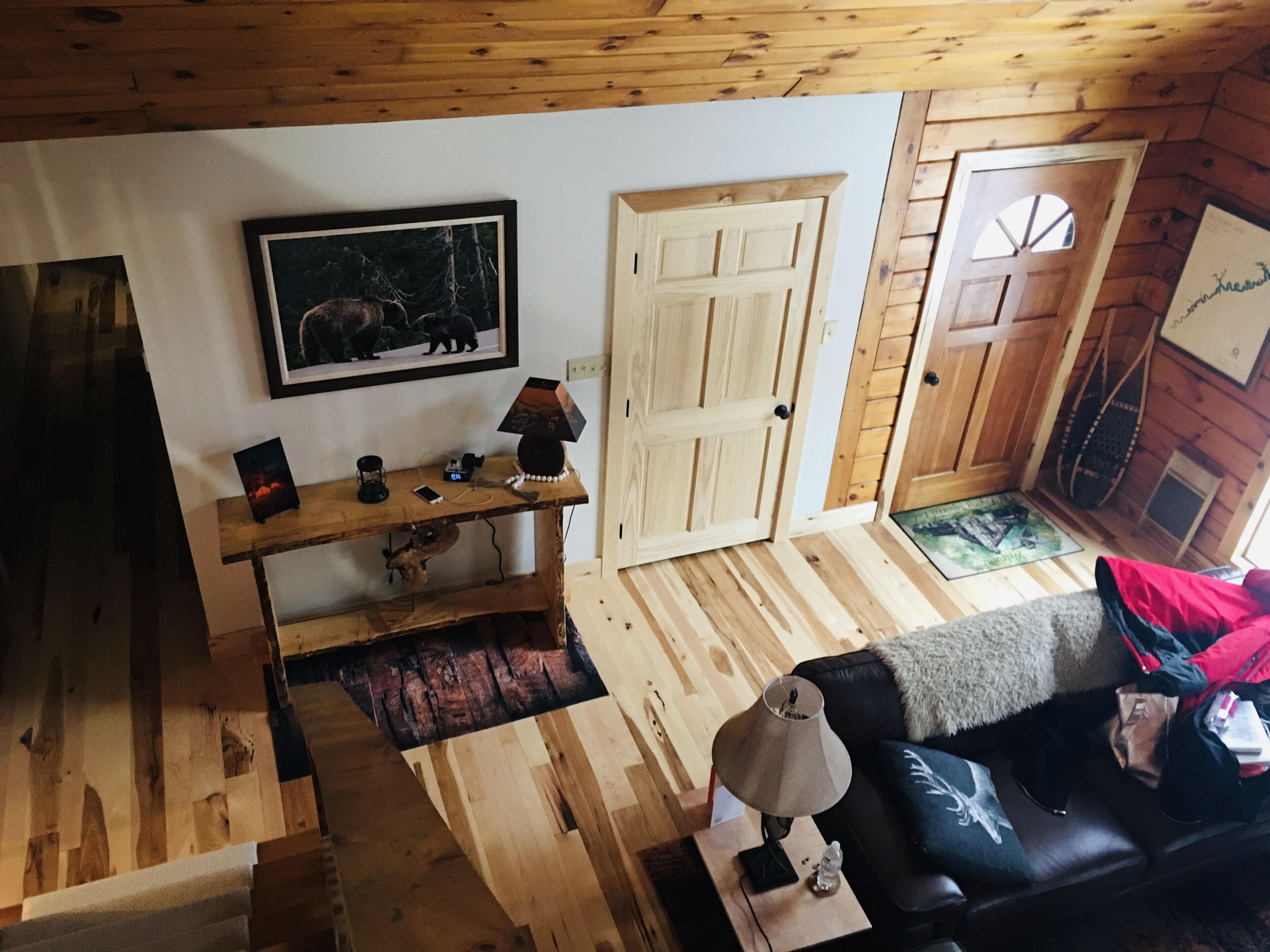 A wooden interior with a black leather sofa, a wooden coffee table, a framed picture, and a door with a window.