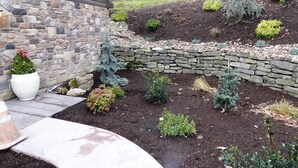 Een aangelegde tuin met een stenen muur, plantenbakken en een kleine kerstboom.