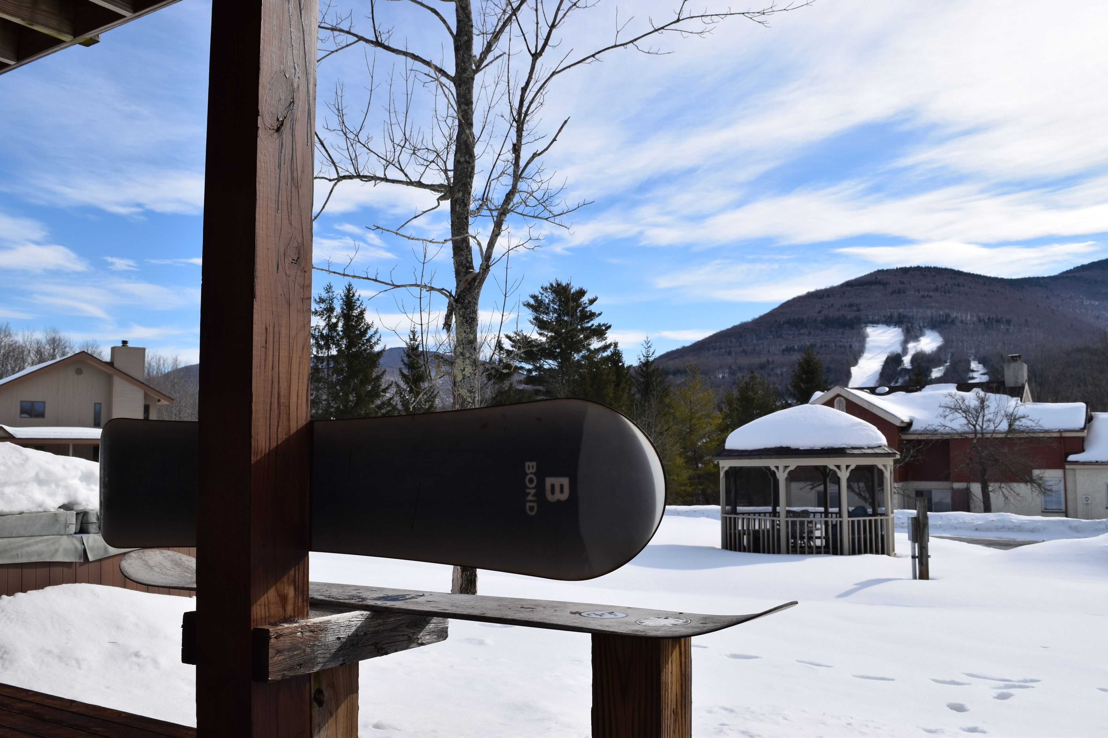A snow-covered deck with a snowboard leaning against a wooden post.