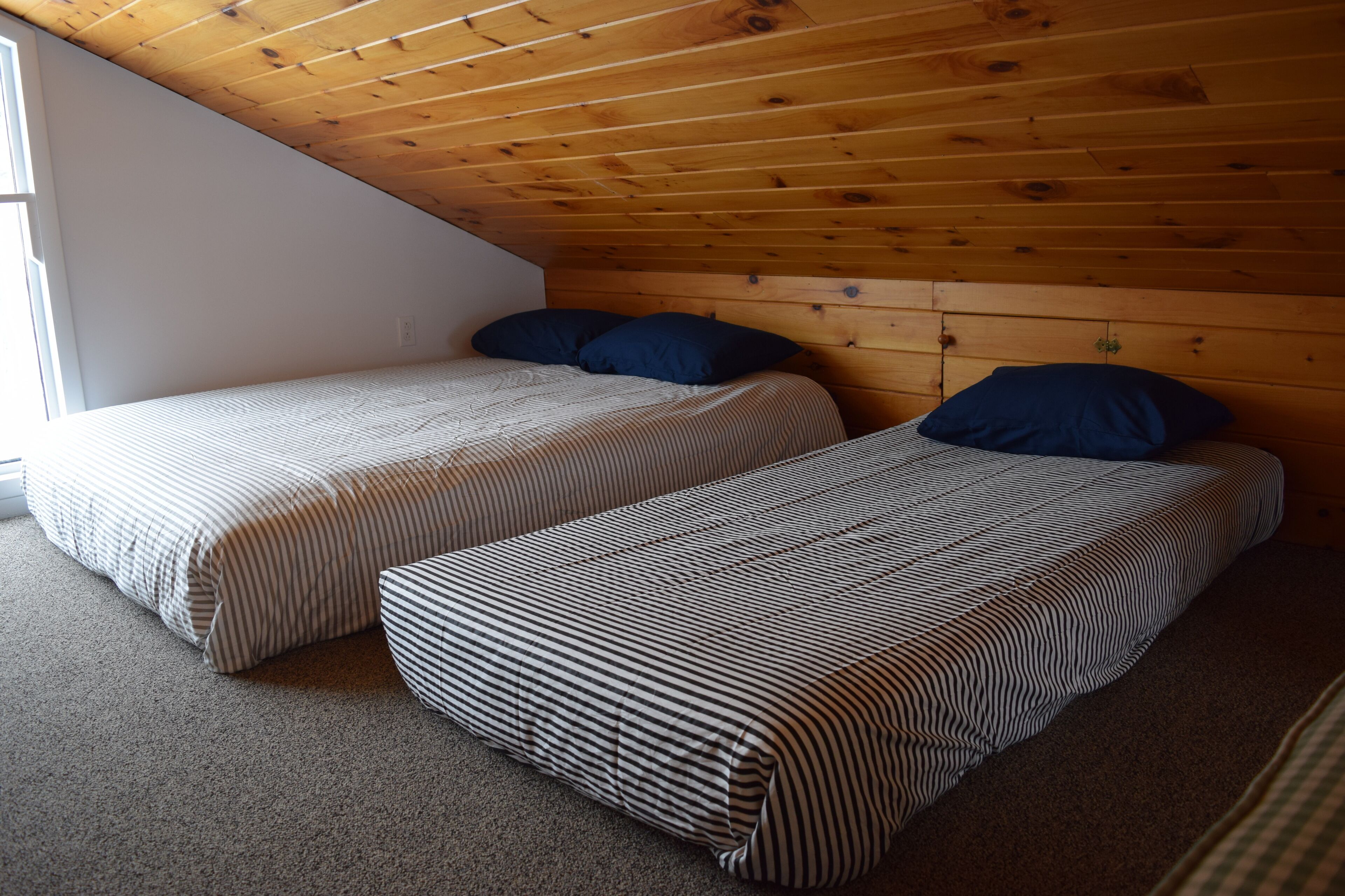 A small, cozy room with two beds, wooden ceiling, and a window.