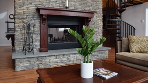 Uma sala de estar com lareira de pedra, escada de madeira e um vaso branco com plantas verdes sobre uma mesa de centro.