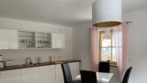 Een moderne keuken met witte kasten, een houten aanrecht en een eethoek met een witte tafel en zwarte stoelen.