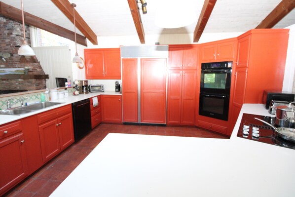 Una cocina con armarios rojos, encimera blanca, pared de ladrillo y techo de madera.