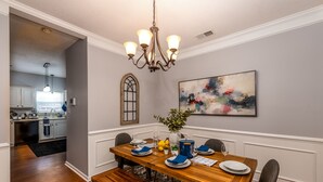 A dining area with a wooden table set for four, a chandelier, a vase with flowers, and a painting on the wall. - Carowinds 2Miles, Fully Fenced Yard, 2,000sq ft House, 5Min Highway (Charlotte)