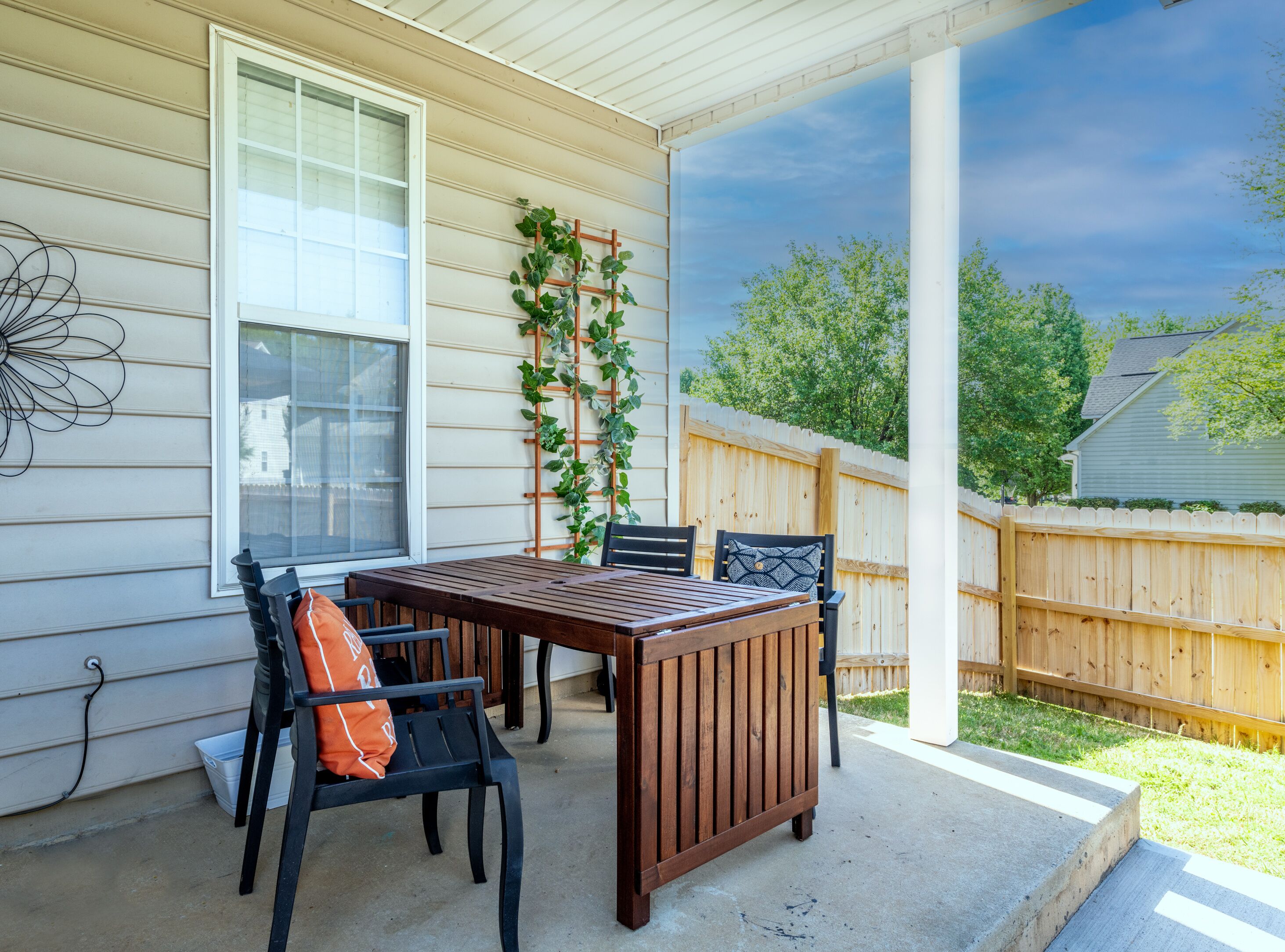 A covered patio with a wooden table and chairs, a white railing, and a wooden fence.