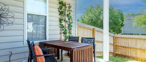 A covered patio with a wooden table and chairs, a white railing, and a wooden fence.