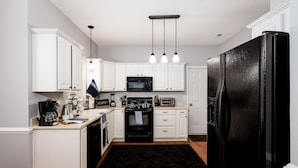 A modern kitchen with white cabinets, a black refrigerator, a microwave, a stove, and a coffee maker. - Carowinds 2Miles, Fully Fenced Yard, 2,000sq ft House, 5Min Highway (Charlotte)