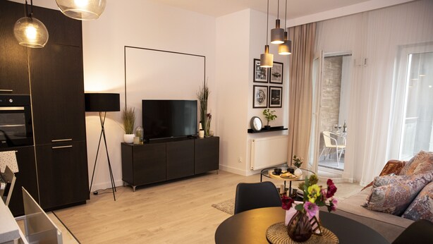 Una sala moderna con un televisor de pantalla plana, armarios de madera oscura, una mesa de comedor con sillas y un sofá con cojines estampados.