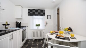 A modern kitchen with white cabinets, a black countertop, and a dining area with a white table and chairs. - Ellie-Jo Cottage (Gardenstown)