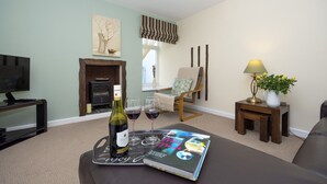 A living room with a fireplace, a television, a magazine, and a bottle of wine. - Ellie-Jo Cottage (Gardenstown)