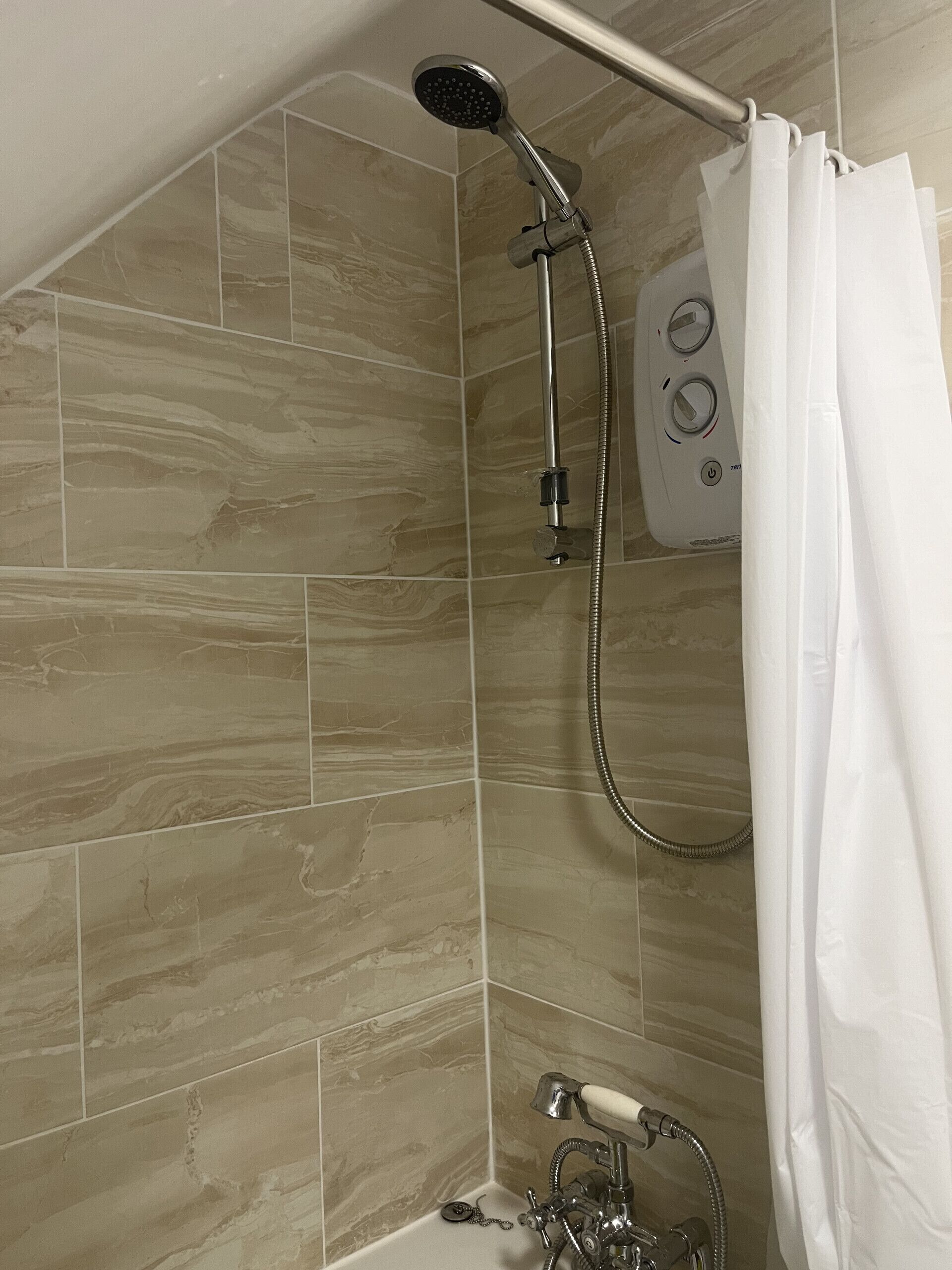 Une douche équipée d’un pommeau de douche à main et d’un panneau de commande fixé au mur.