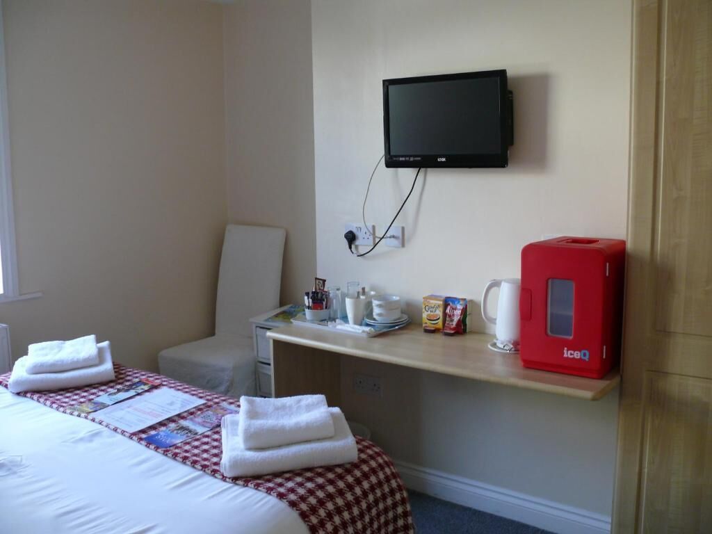 A hotel room with a bed, a desk with a television, a chair, and a red ice machine.