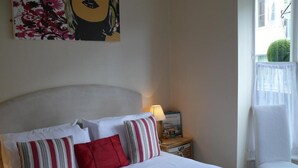 A hotel room with a bed, pillows, a nightstand with a lamp, a chair, and a window with a view of a building and a tree. - Bow Street Runner (Hove)