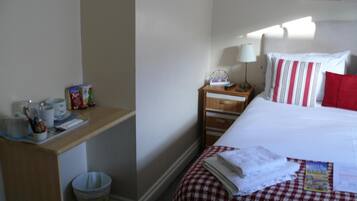 A hotel room with a bed, a bedside table with a lamp, a small trash bin, and a window with a view.