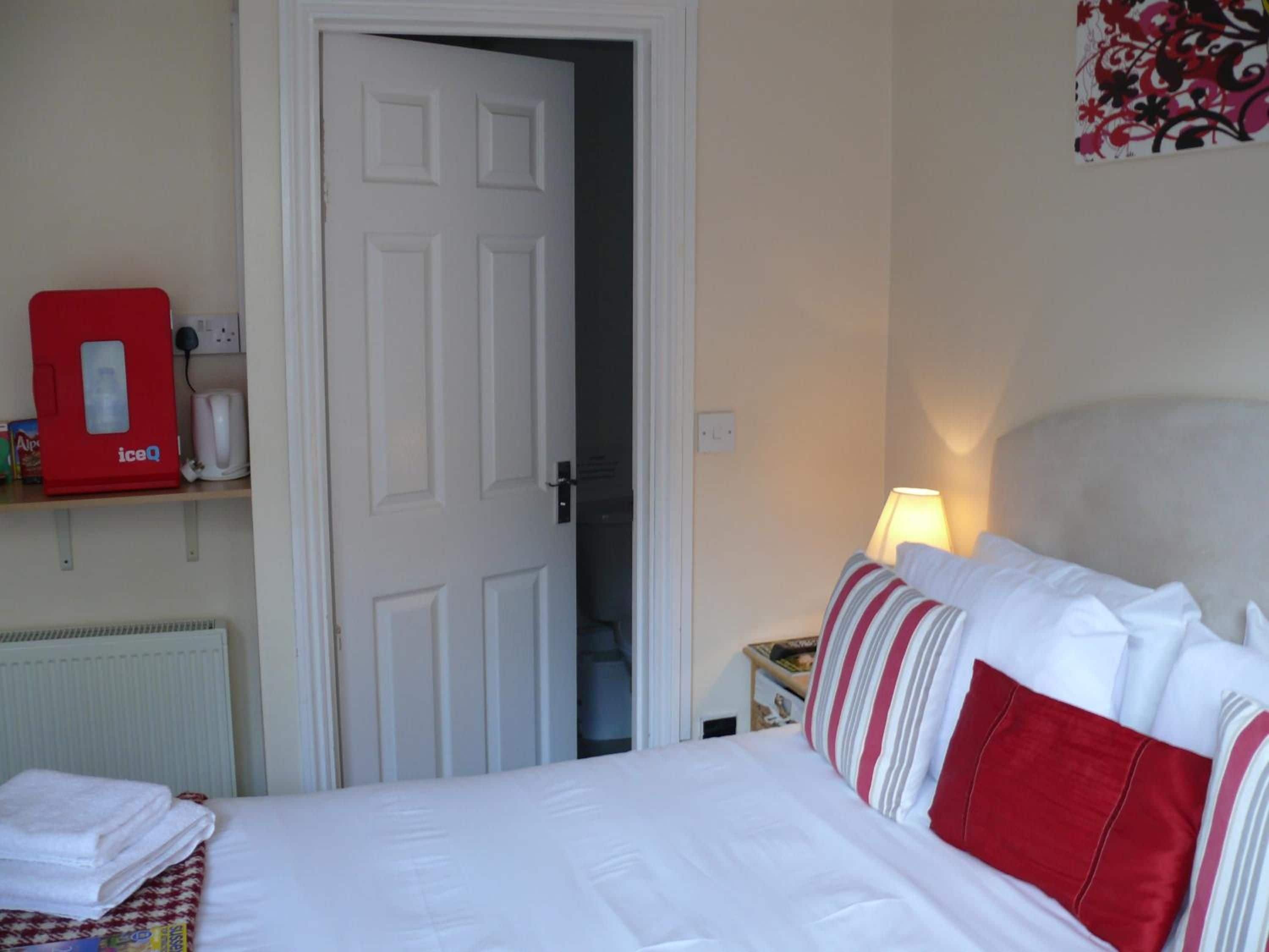 Una camera d'albergo con un letto, un comodino con una lampada, una macchina per il ghiaccio rossa e una porta che conduce a un'altra stanza.