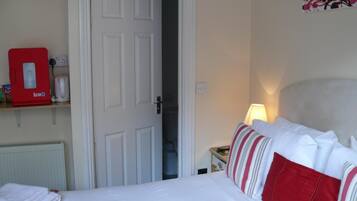 A hotel room with a bed, a nightstand with a lamp, a red ice machine, and a door leading to another room.