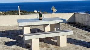 Un tavolo da patio con una bottiglia di vino e bicchieri, con vista sulla costa.