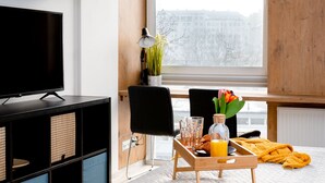 A modern hotel room with a bed, a TV, a wooden side table with breakfast items, a chair, and a view of a snowy cityscape. - Easy Rent Nieruchomości - SMART 316 (Lublin)