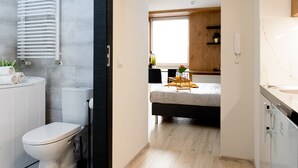 A compact hotel room with a modern bathroom, a bed with a bedside table, and a small window. - Easy Rent Nieruchomości - SMART 316 (Lublin)