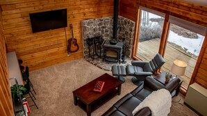 A cozy cabin interior with a stone fireplace, leather sofas, a wooden TV wall, and a guitar. - 3BR Pet Friendly | Mountain Views, Dark Skies, Walk to Trails, Exceptional Coffee (Pagosa Springs)