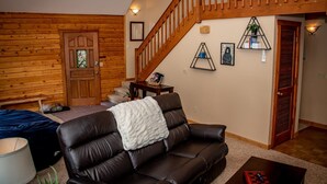 A cozy living room with a leather sofa, a wooden staircase, and a door leading to another room. - 3BR Pet Friendly | Mountain Views, Dark Skies, Walk to Trails, Exceptional Coffee (Pagosa Springs)