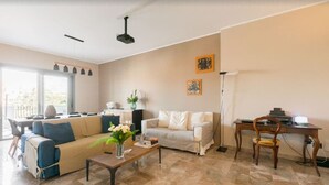 Ein modernes Wohnzimmer mit Sofa, Couchtisch und Schreibtisch. Ein Fenster sorgt für Tageslicht und bietet einen Blick ins Freie.