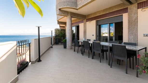 Ein Balkon mit Essbereich, Meerblick und einem Gebäude mit strukturierter Fassade.