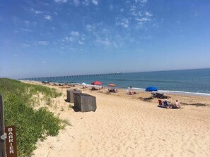 A beach with a pier in the background, beach umbrellas, and people relaxing. - BIS-Duck Resort - Large 3BR/3BA - Great Pools and Beach! (Duck)