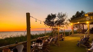 An outdoor seating area with wooden chairs and tables, overlooking a body of water during sunset. - BIS-Duck Resort - Large 3BR/3BA - Great Pools and Beach! (Duck)