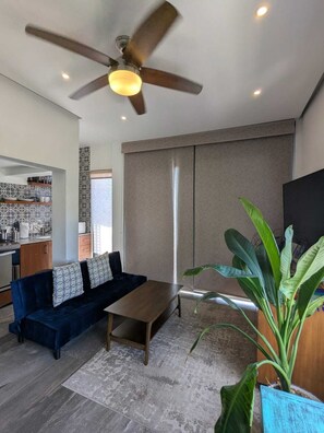 A modern living room with a dark blue sofa, a wooden coffee table, a ceiling fan, and a large green plant. - 5D Area! Modern New, 1Bd 1Ba Rooftop Pool (Puerto Vallarta)