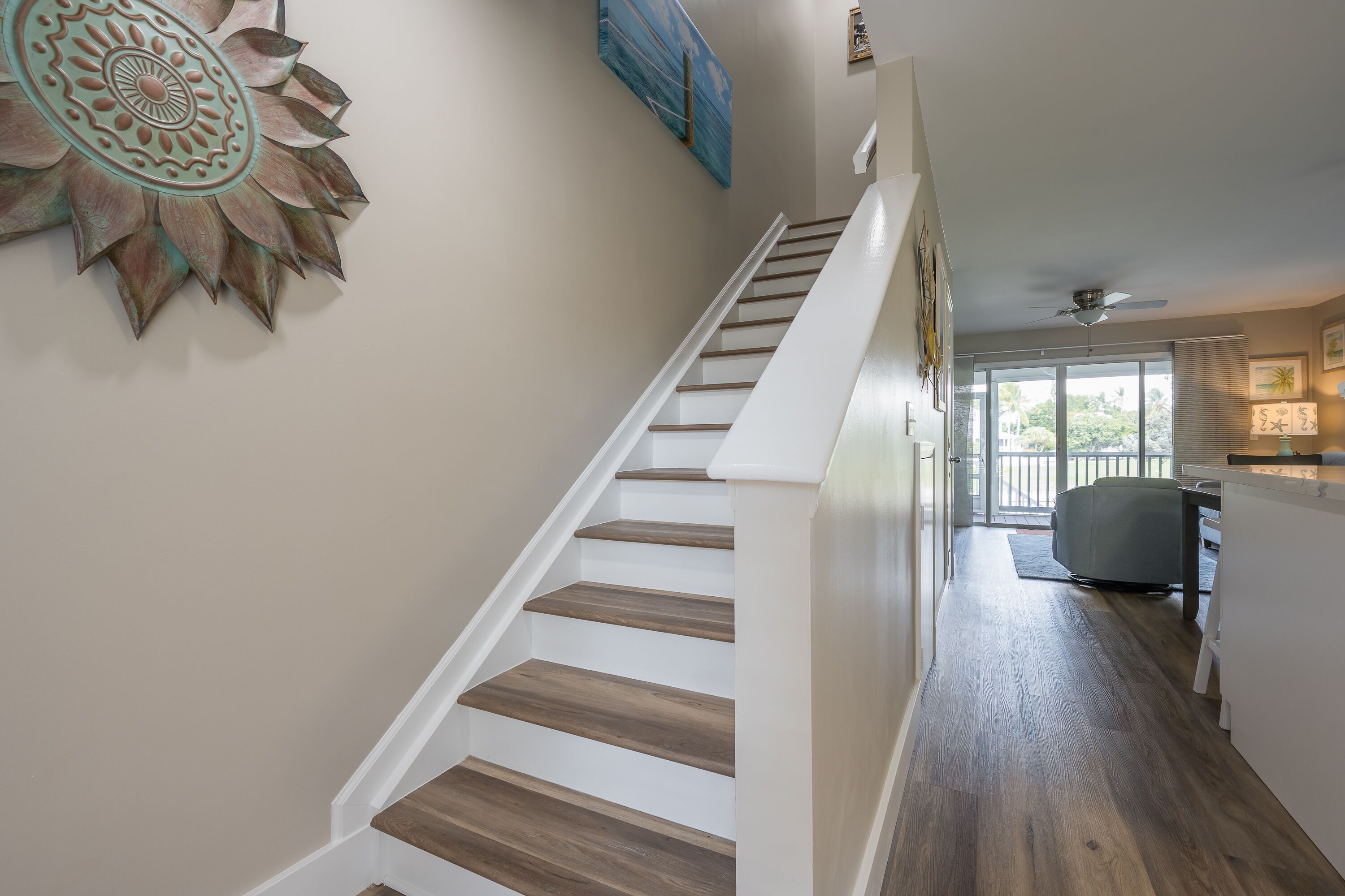 A staircase with wooden steps and white railings, leading to a room with a view of the outdoors.