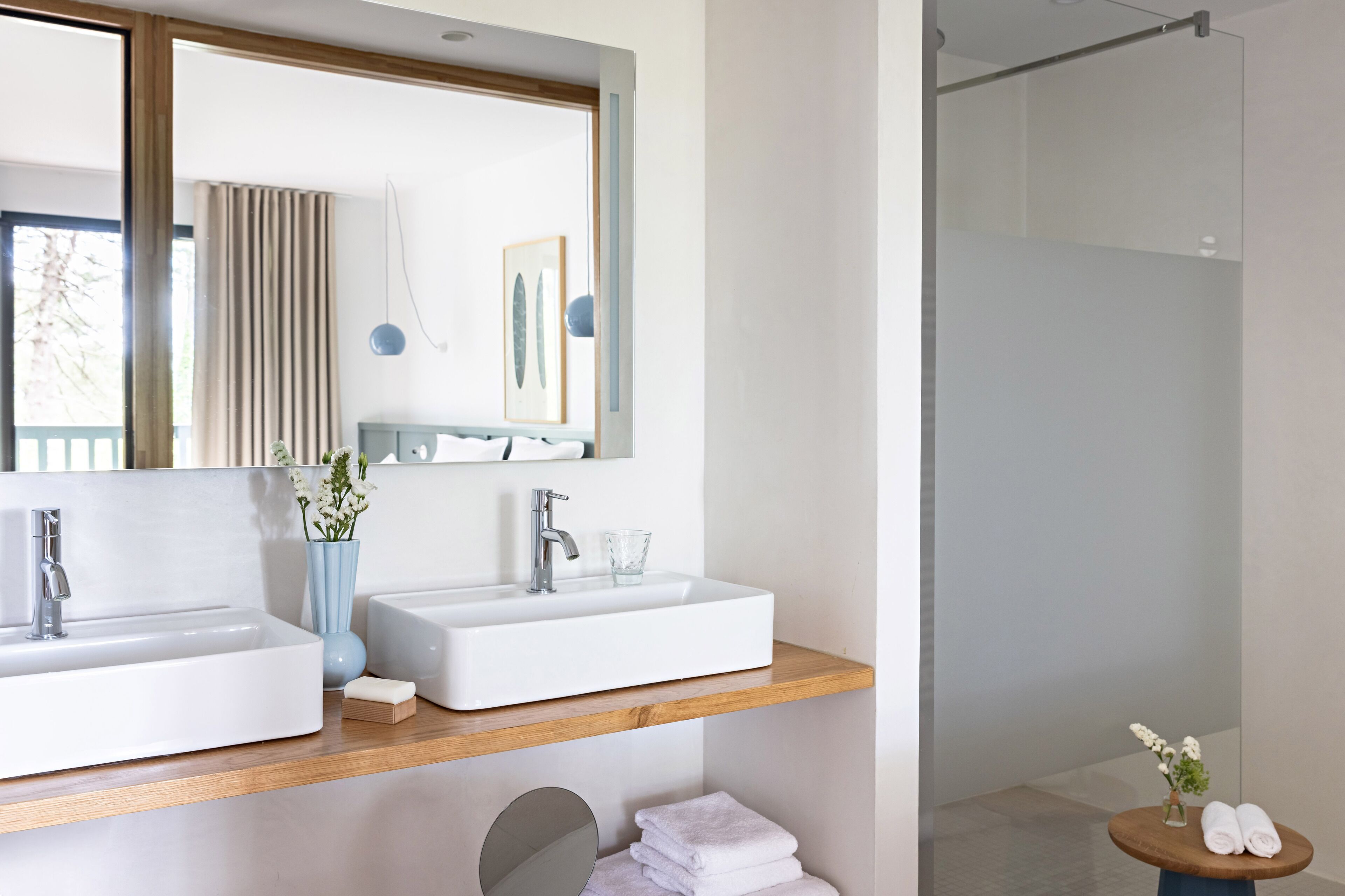 A modern bathroom with two sinks, a mirror, a shower, and a round table with towels.