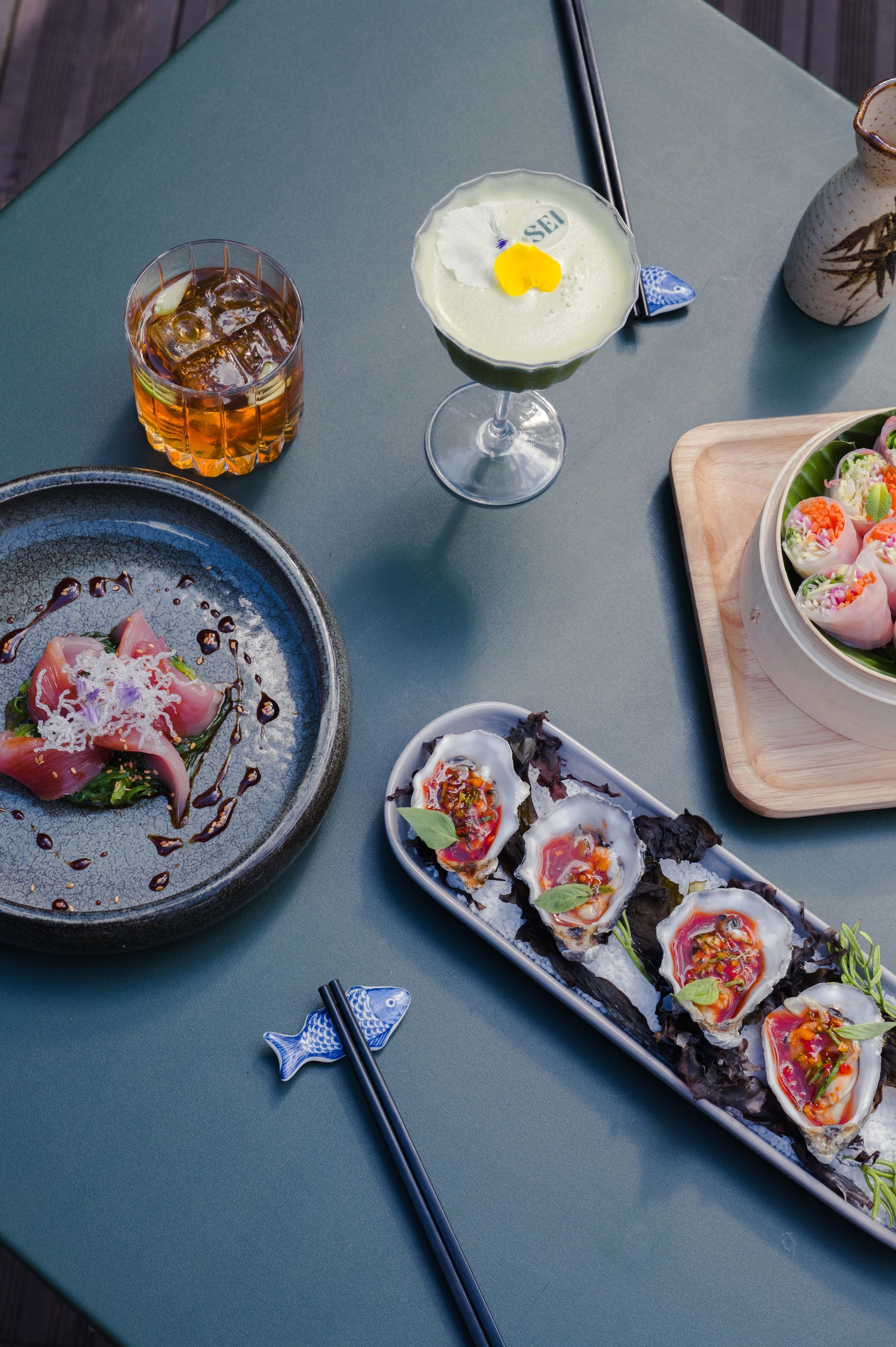 A table with various dishes, including sushi, a cocktail, and a glass of beer.
