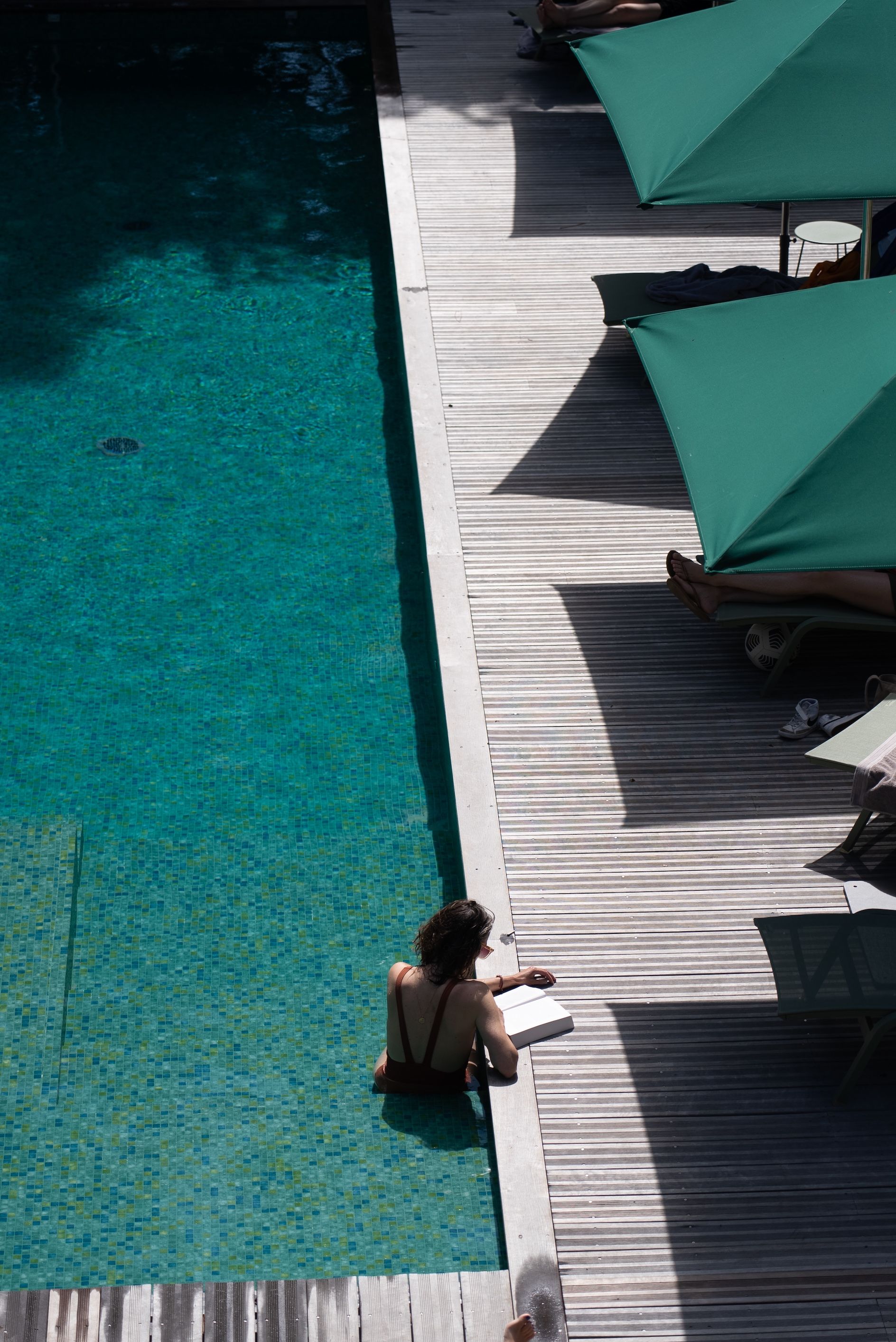 A poolside area with a wooden deck, lounge chairs, and umbrellas.