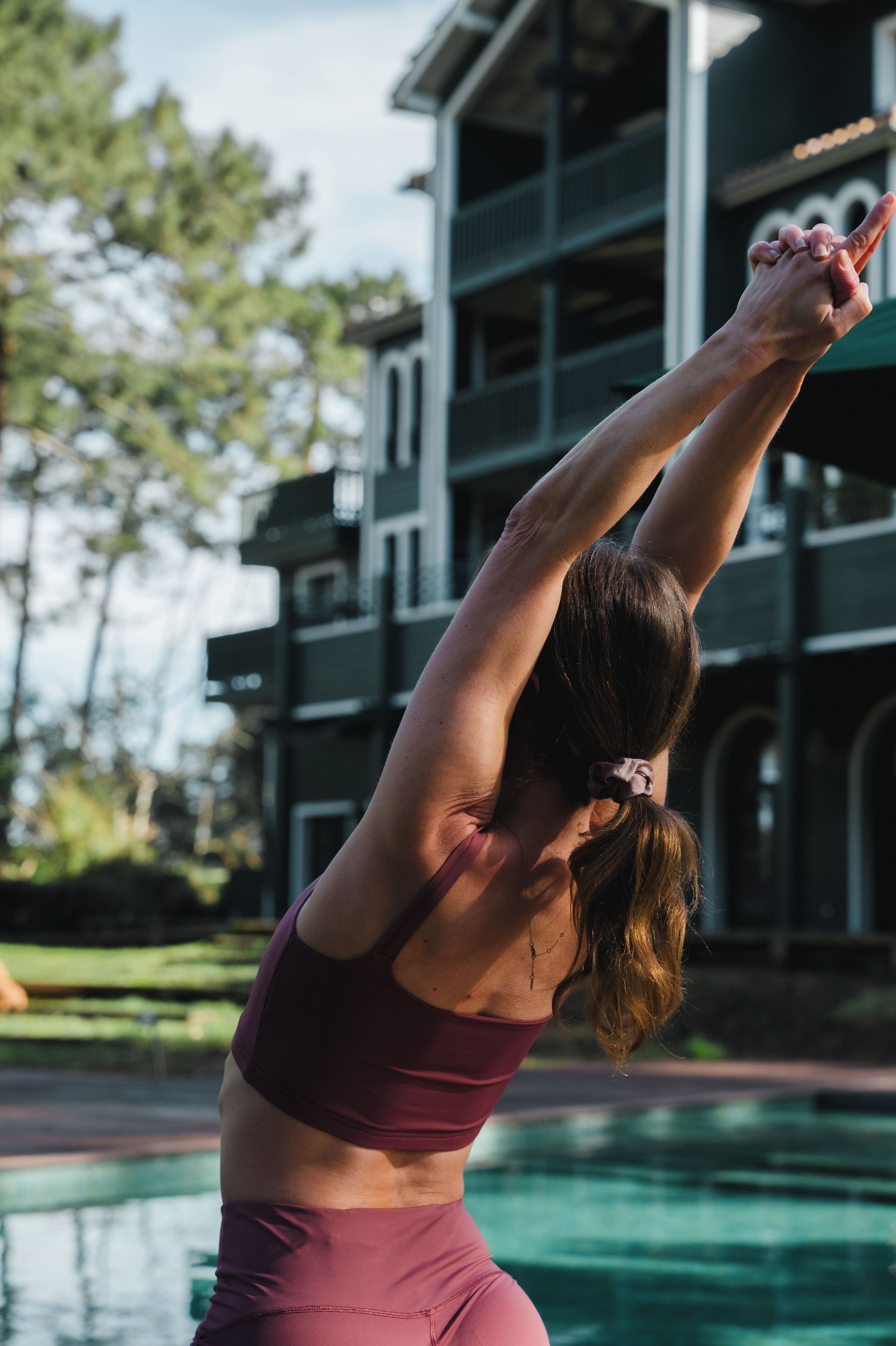 A person performing a yoga pose by a swimming pool with a building in the background.