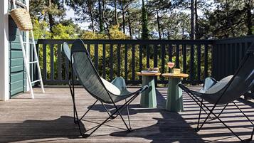 Eine Terrasse mit zwei Liegestühlen, einem kleinen Tisch mit Getränken und einem Korbwäscher auf einem Holzboden.