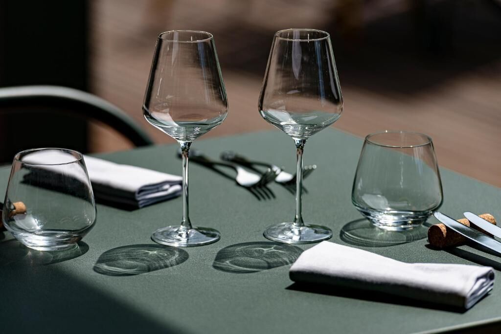Una mesa con cuatro copas de vino vacías, una servilleta doblada y un sacacorchos sobre un mantel verde.
