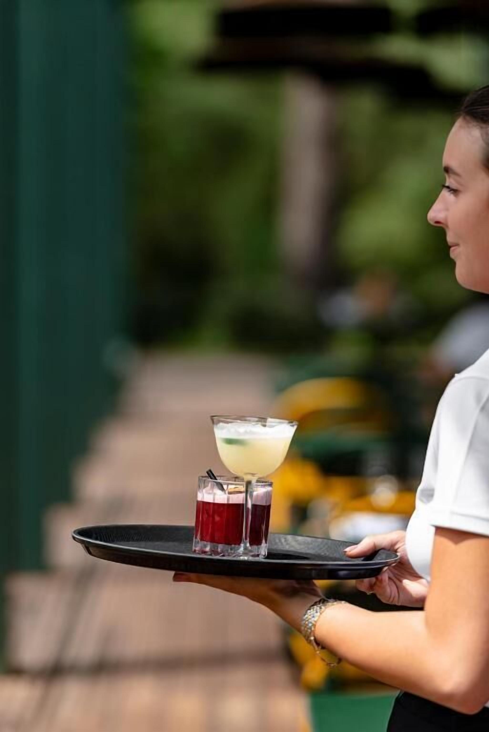 Une personne tenant un plateau sur lequel se trouvent une boisson et un verre.