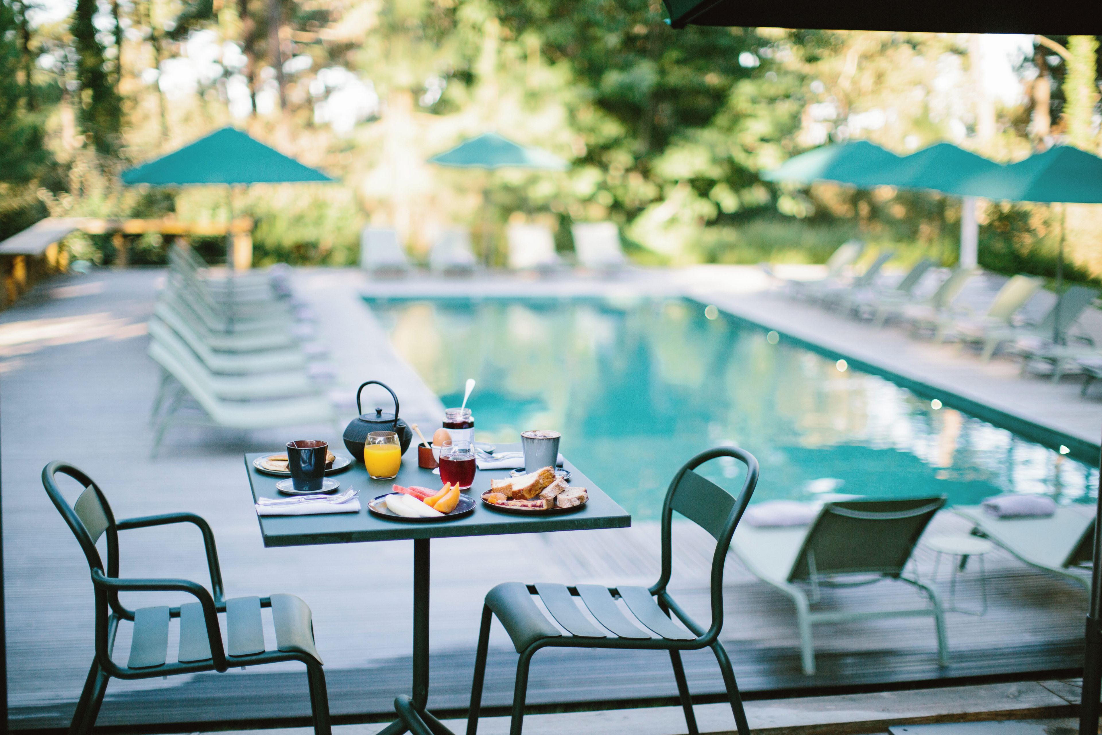 A poolside dining area with a table set for two, surrounded by lounge chairs.
