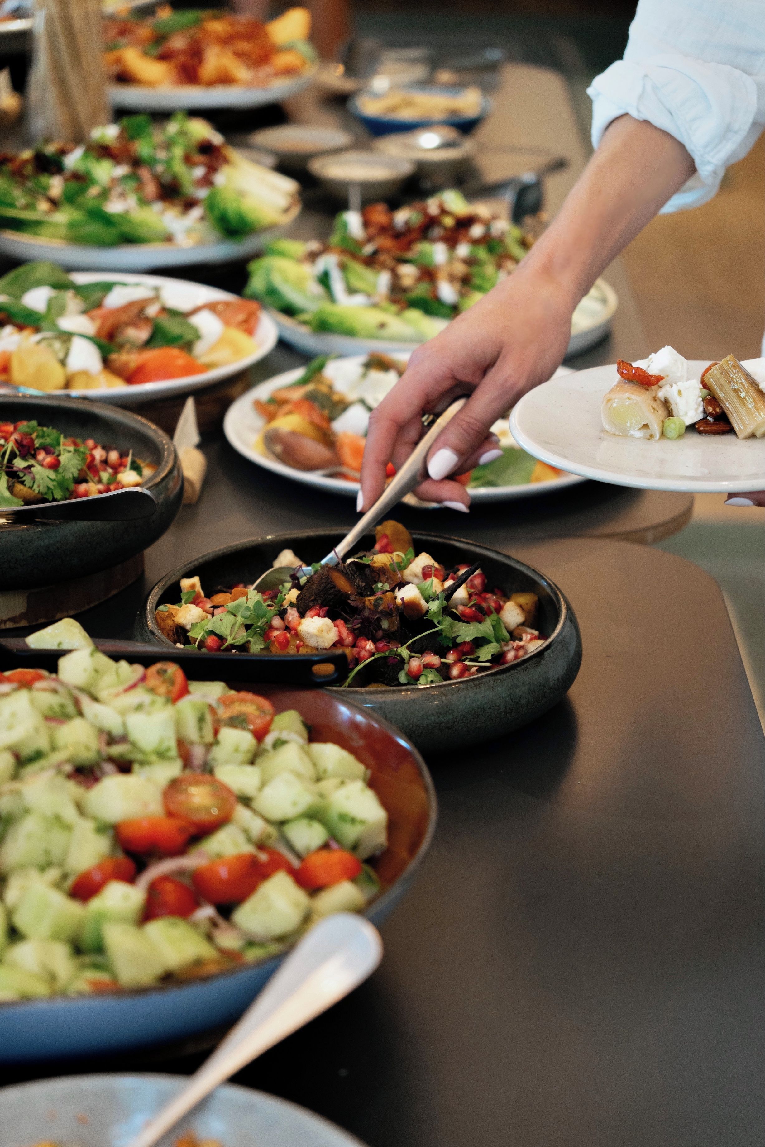 Une table de buffet proposant divers plats, notamment des salades, et une personne qui sert les aliments.