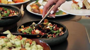 Une table de buffet proposant divers plats, notamment des salades, et une personne qui sert les aliments.