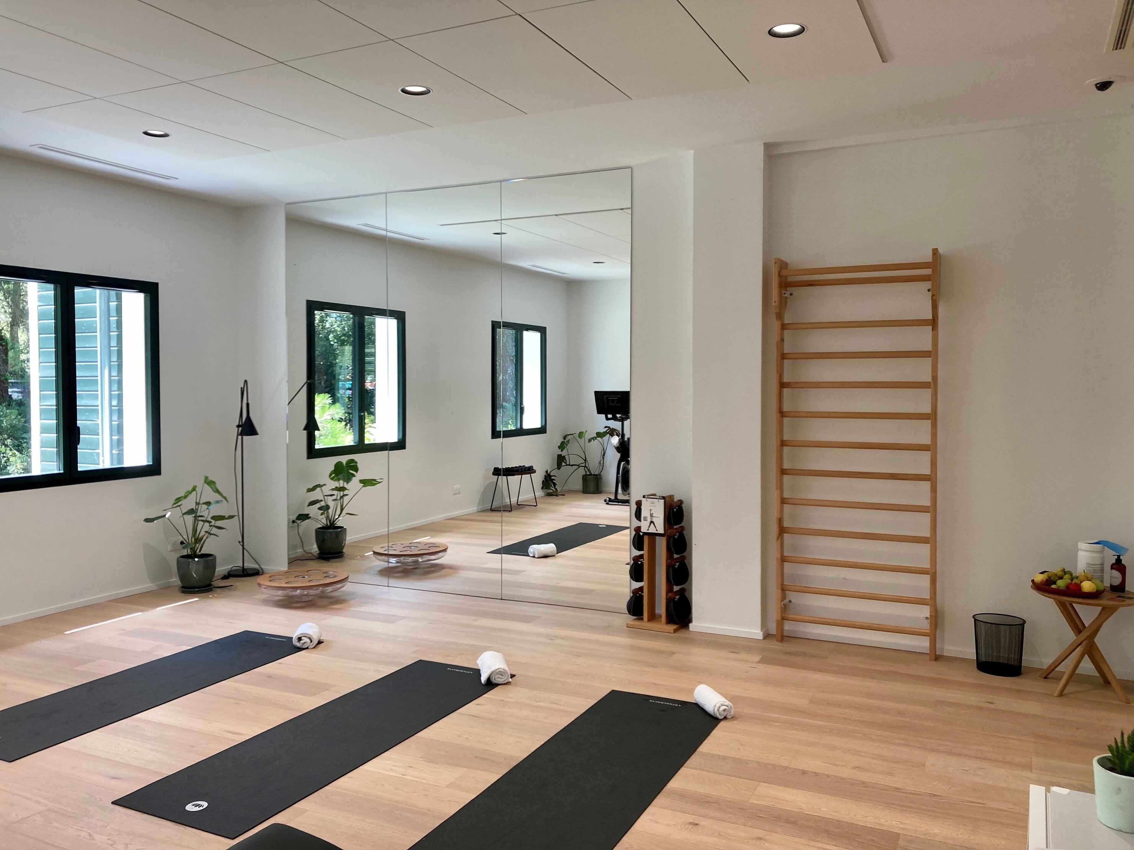 Una habitación amplia con grandes ventanales, suelo de madera y colchonetas de yoga dispuestas en el piso.