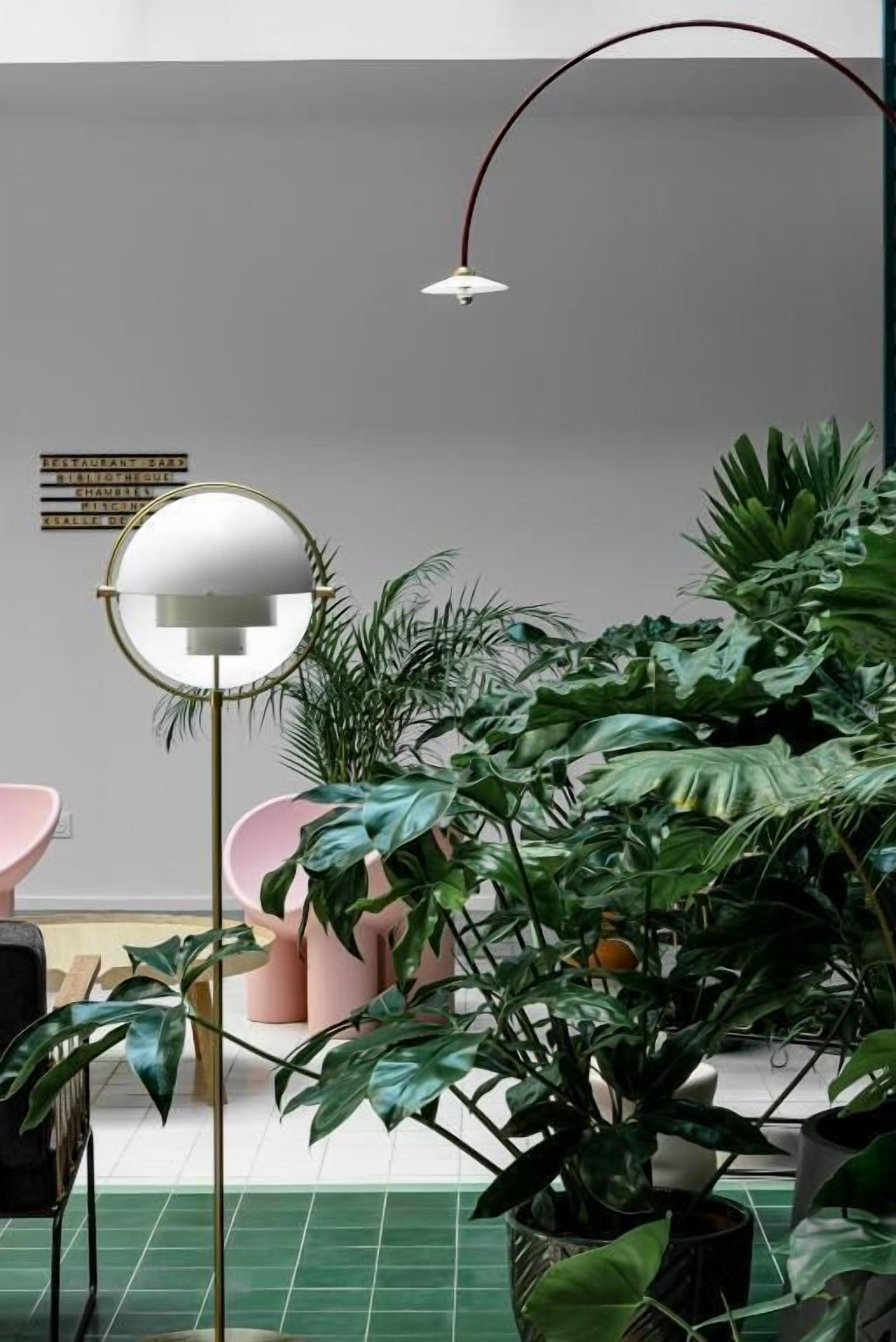 Una habitación con un espejo redondo, plantas verdes y sillas rosas.