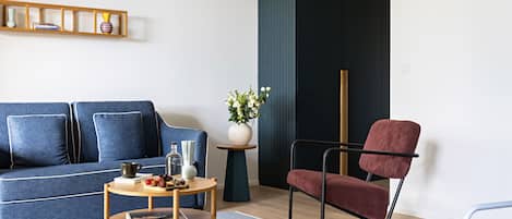 A modern living room with a blue sofa, a red chair, a small wooden table, and a vase with flowers.