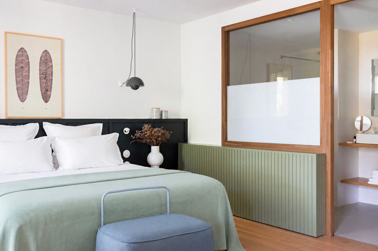 A modern bedroom with a bed, bedside table, lamp, and a large mirror.