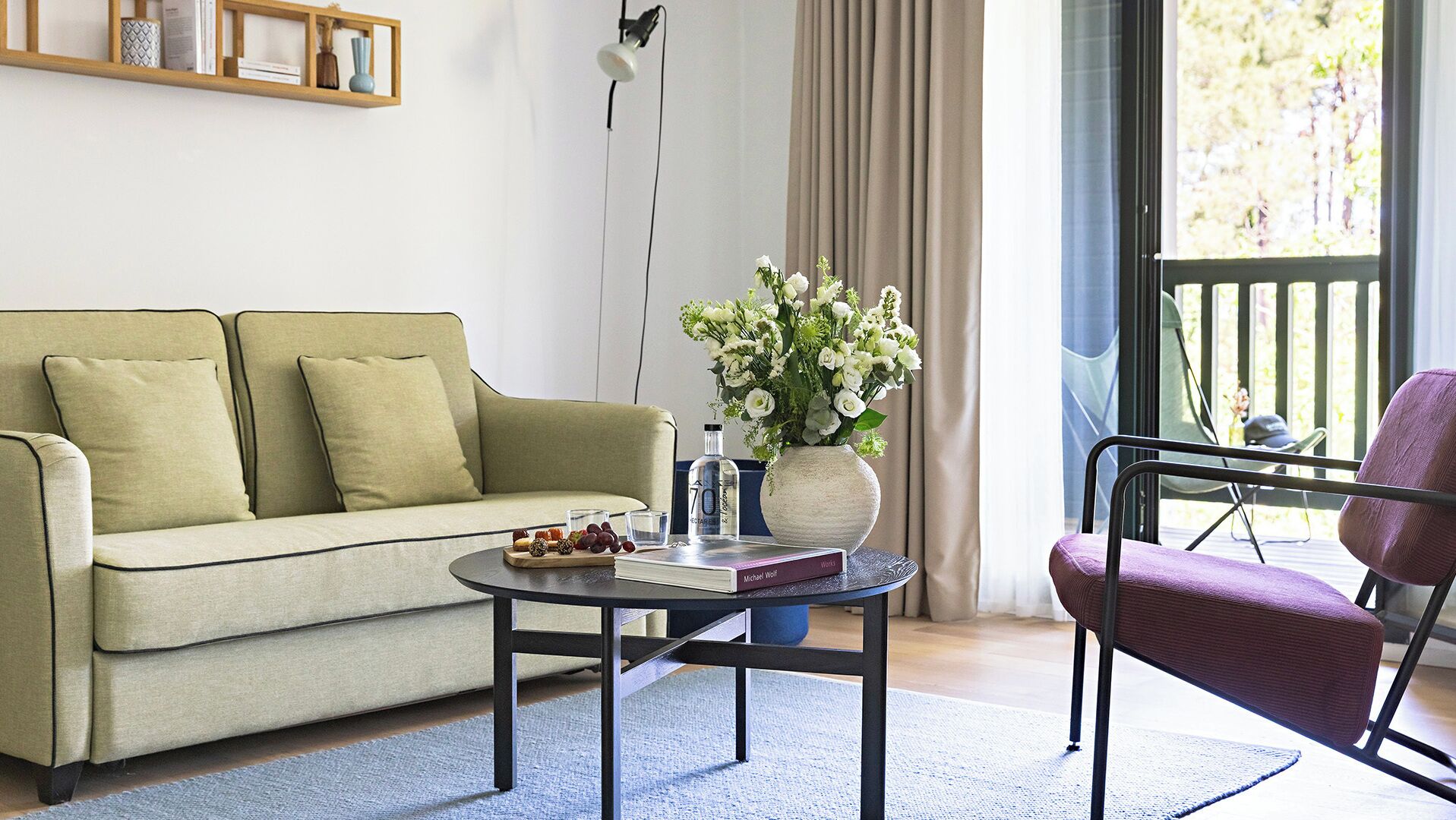 Una sala de estar con sofá, mesa de centro, sillón, un jarrón con flores y estantería.