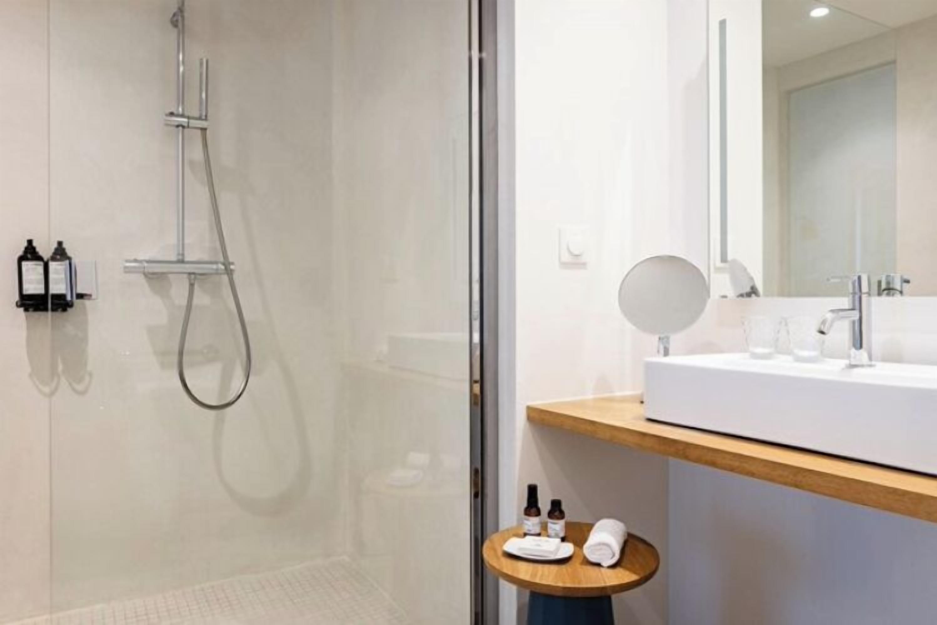 A modern bathroom with a glass-enclosed shower, a white sink with a wooden countertop, and a round mirror.