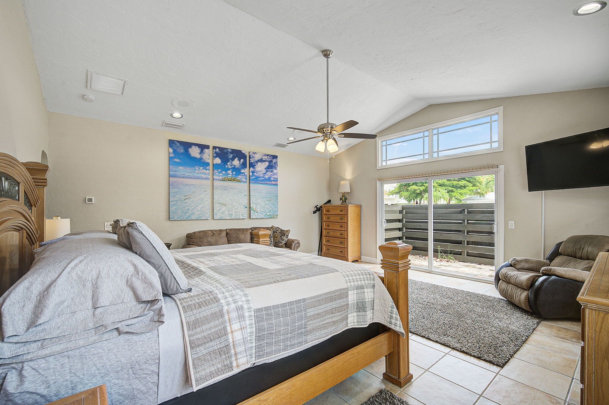 A bedroom with a bed, a ceiling fan, a window, and a TV.